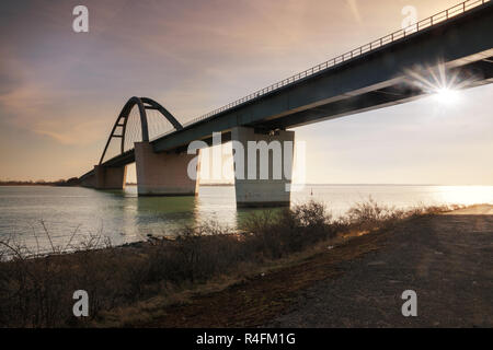 Fehmarn Sound Bridge im Sonnenuntergang (Deutsch: fehmarnsundbrücke), Suspension Bridge mit Stahlbögen Anschließen der deutschen Festland mit der Insel in der Stockfoto