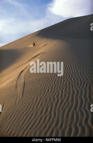 Man Boarding nach unten eine große Sanddüne in der Wüste. Stockfoto