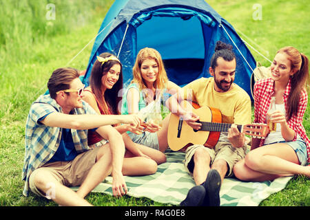 Glückliche Freunde mit Getränken und Gitarre am camping Stockfoto