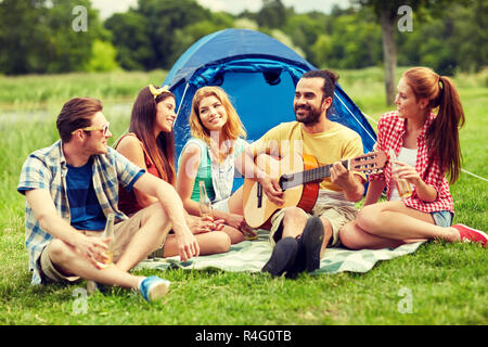 Glückliche Freunde mit Getränken und Gitarre am camping Stockfoto