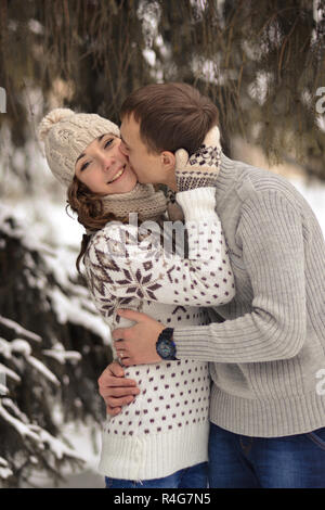 Schöner mann Kuss auf die Stirn, ihren Geliebten, schön, hübsch, fröhlich, romantisch, verliebt, lächelnde Mädchen mit dem Pullover, Handschuhe und Hut, im Winter, Schnee, kalten Wald, wahre Liebe in gefrorenem, winter, wald, Paar, zärtlich, aufmerksam, fürsorglich, Beziehung, Affäre Stockfoto