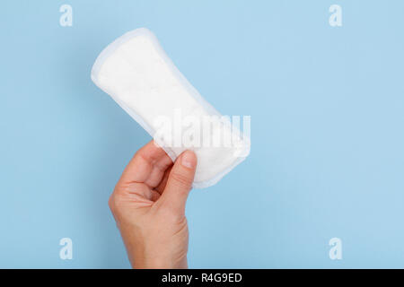 Weiß sanitär Pad in der Hand der Frau auf einem blauen Hintergrund. Absorbierendes Element für Frauen besondere Tage. Hygiene und Gesundheit Konzept. Stockfoto