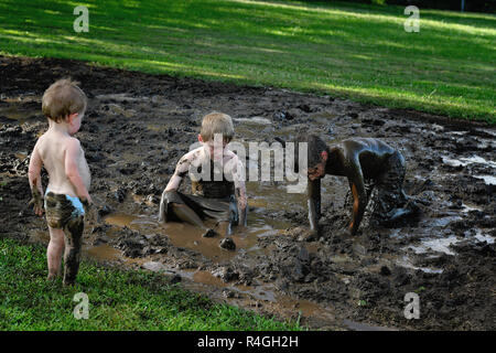 Jungen spielen im Schlamm, während Baby Bruder in eine Windel Uhren von der Kante der Schlamm Grube Stockfoto