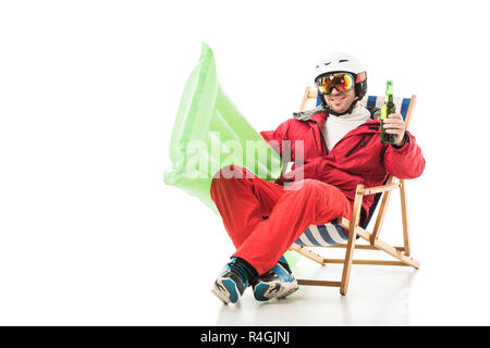 Mann in Ski Kleidung mit Bierflasche und pool Matratze sitzt im Liegestuhl und lächelnd auf Weiß isoliert Stockfoto