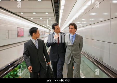 Drei Kollegen sprechen auf einer Rolltreppe. Stockfoto
