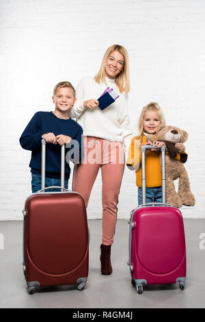 Happy Mother holding Passport und Tickets während die Kinder holding Koffer bereit, auf Winter Reise zu gehen Stockfoto