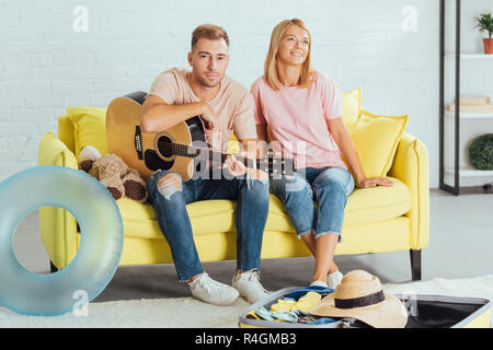 Mann mit Gitarre, während Frau träumen über Sommerferien und auf der Couch zu Hause sitzen Stockfoto