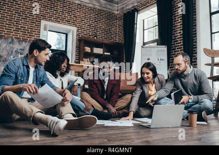 Multiethnische Gruppe von colworkers sitzen auf dem Boden und gemeinsam diskutieren neues Projekt in der modernen Loft Büro Stockfoto
