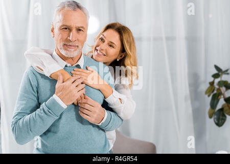 Glückliche Ehefrau umarmen reifer Mann von hinten zu Hause Stockfoto