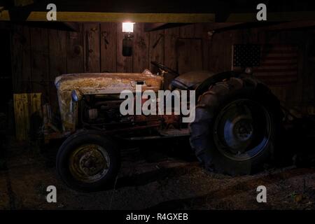 Ein vintage oder antike Traktor in einer alten Scheune unter dem Licht einer Laterne. Stockfoto