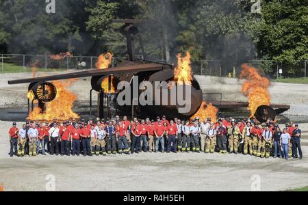 Teilnehmer und Feuerwehrmänner posieren für ein Gruppenfoto vor einem brennenden Ausbildung Flugzeuge am Ende der Brand Ops 101 Veranstaltung in Wright-Patterson Air Force Base, Ohio, Sept. 28, 2018. Die Veranstaltung erlaubt Base und lokalen Entscheidungsträgern eine Chance zu sehen, die neuesten Produkte ihrer Feuerwehren sind und was Sie tun, auf einer täglichen Basis. Stockfoto