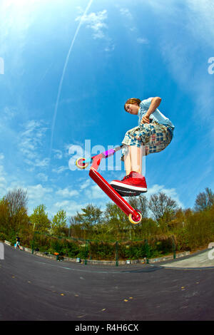 Junge springt mit einem Motorroller über einen Dorn in den Skate Park Stockfoto