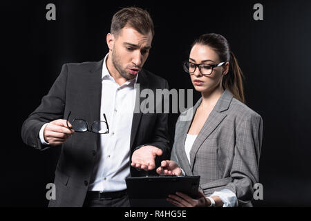 Junge Geschäftsleute mit Zwischenablage in Gespräch isoliert auf Schwarz Stockfoto