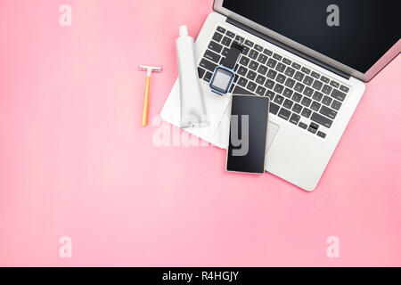 Der Mensch stopft wie Laptop, erobert, Mobiltelefon, gelb Rasierer und Zahnpasta Produkt für Reisen auf rosa Hintergrund. Ansicht von oben Stockfoto