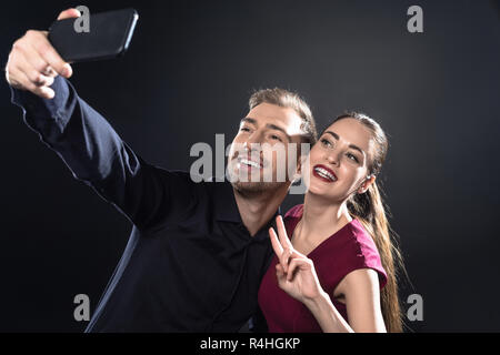Glückliches junges Paar unter selfie mit Smartphone isoliert auf Schwarz Stockfoto