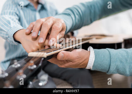 Zugeschnittenes Bild des Menschen lehren Kinder spielen auf der Akustikgitarre zu Hause Stockfoto