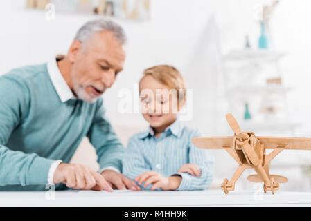 Selektiver Fokus reifer Mann, Paper Plane, während seine adorable Enkel Sitzen am Tisch mit dem Flugzeug Stockfoto