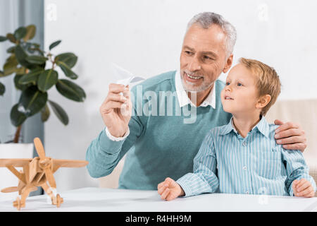 Lächelnd reifer Mann und Enkel Spaß mit Paper Plane zu Hause Stockfoto