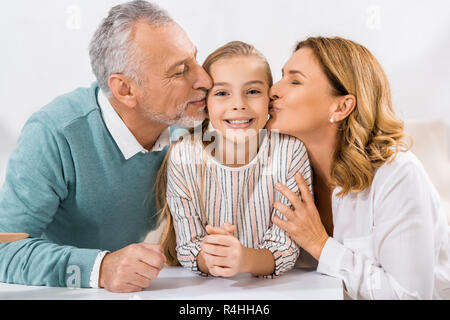 Adorable Kind an der Kamera, während die Großeltern ihr Küssen in Wangen Stockfoto