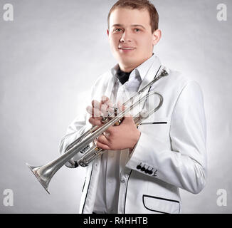 Junge Mann in einem weißen Anzug mit einer Trompete. auf schwarzem Hintergrund Stockfoto