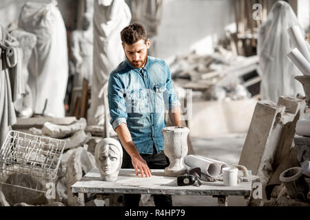 Porträt einer stattlichen Bildhauer in blauen T-Shirt und Schürze arbeiten mit Skulpturen aus Stein auf dem Tisch an der alten atmosphärischen Studio Stockfoto
