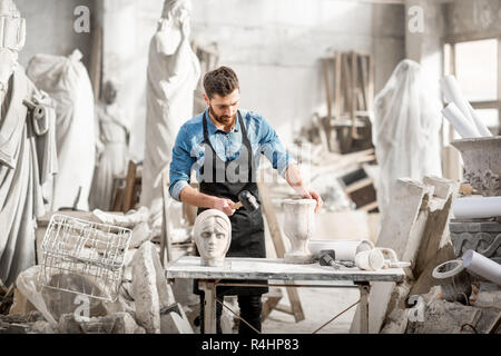 Porträt einer stattlichen Bildhauer in blauen T-Shirt und Schürze arbeiten mit Skulpturen aus Stein auf dem Tisch an der alten atmosphärischen Studio Stockfoto