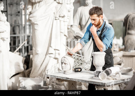 Porträt einer stattlichen Bildhauer in blauen T-Shirt und Schürze arbeiten mit Skulpturen aus Stein auf dem Tisch an der alten atmosphärischen Studio Stockfoto