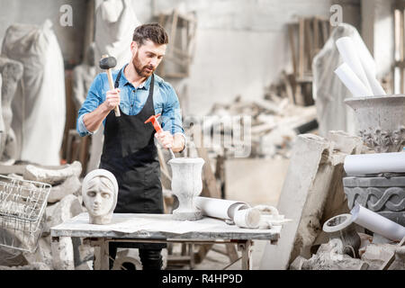 Porträt einer stattlichen Bildhauer in blauen T-Shirt und Schürze arbeiten mit Skulpturen aus Stein auf dem Tisch an der alten atmosphärischen Studio Stockfoto