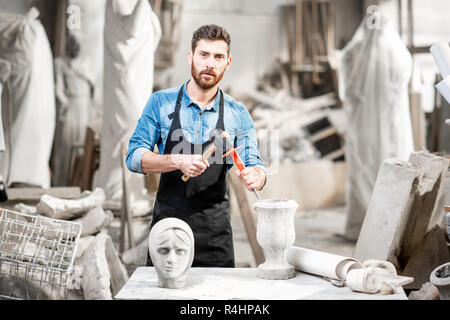 Porträt einer stattlichen Bildhauer in blauen T-Shirt und Schürze arbeiten mit Skulpturen aus Stein auf dem Tisch an der alten atmosphärischen Studio Stockfoto