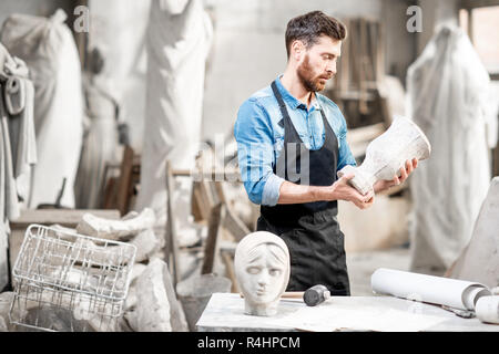 Porträt einer stattlichen Bildhauer in blauen T-Shirt und Schürze holding Stein Vase in der Alten atmosphärischen Studio Stockfoto