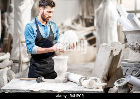 Porträt einer stattlichen Bildhauer in blauen T-Shirt und Schürze holding Stein Vase in der Alten atmosphärischen Studio Stockfoto