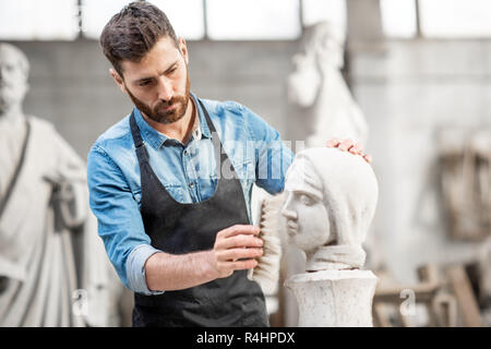 Stattliche Bildhauer bürsten Steinkopf Skulptur auf dem Tisch in der atmosphärischen Studio Stockfoto