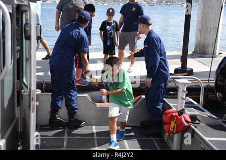 Feuerwehrmann Patrick Saragossa und Feuerwehrmann Falcon Piner, Coast Guard Station San Diego, helfen die jungen Gäste an Bord eines 33-Fuß-Special Purpose Handwerk - Strafverfolgung, während einer Open House bei Coast Guard Sektor San Diego Okt. 28, 2018. Die Open House war in Verbindung mit Fleet Week San Diego statt und wurde der Gemeinschaft die Möglichkeit, sich mit ihren lokalen Küstenwache zu interagieren. Stockfoto