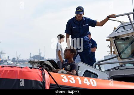 Feuerwehrmann Patrick Saragossa, Coast Guard Station San Diego, zeigt eine junge Besucher der Bug eines 33-Fuß-Special Purpose Handwerk - Strafverfolgung, während einer Open House bei Coast Guard Sektor San Diego Okt. 28, 2018. Die open house wurde der Gemeinschaft die Möglichkeit, verschiedene Vermögenswerte, die von der Küstenwache verwendet und Partneragenturen zu sehen maritime Missionen durchzuführen. Stockfoto