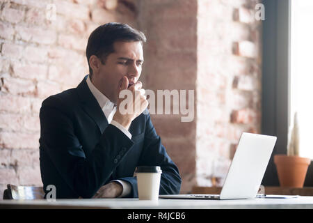 Müde Geschäftsmann deckt seinen Mund mit seiner Hand beim Gähnen. Stockfoto