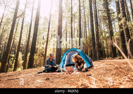 Zwei verschiedene Altersgruppen kaukasische Frau in sich zusammen, Camping in den Pinien Wald essen ein Sandwich - Freiheit und Unabhängigkeit für erwachsene Menschen - altern Stockfoto