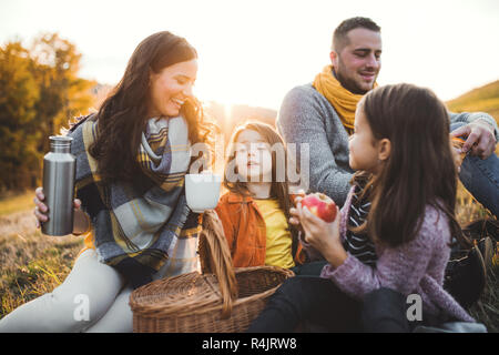 Eine junge Familie mit zwei kleinen Kindern in Picknick im Herbst Natur bei Sonnenuntergang. Stockfoto