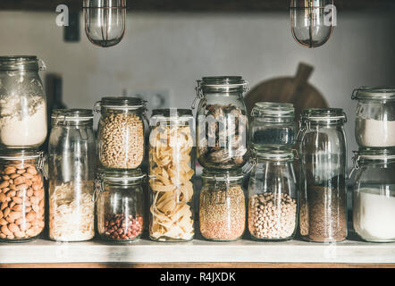 Rustikale Küche essen Lageranordnung. Verschiedene Getreide, Müsli, Nüsse, Trockenfrüchte, Mehl und Pasta Arten in Gläsern auf Beton Arbeitsplatte in der Küche. Stockfoto