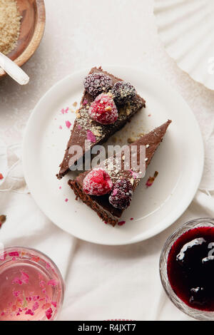 Zwei Stücke Schokolade Käsekuchen mit Himbeeren auf einer weißen Platte auf einem Tisch mit weißen Tischtüchern bedeckt Vintage Stockfoto