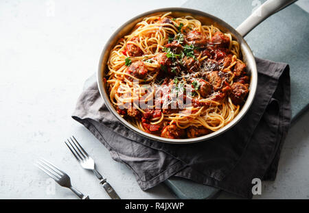 Spaghetti mit Fleischbällchen, Tomatensauce, Petersilie und Käse in einer Pfanne auf weißem Beton Hintergrund serviert. Stockfoto