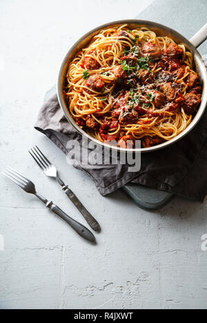 Spaghetti mit Fleischbällchen, Tomatensauce, Petersilie und Käse in einer Pfanne auf weißem Beton Hintergrund serviert. Stockfoto