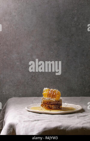 Bio Honig in den Waben in beschmutzt Keramikplatte auf Leinen Tischdecke mit grauen Wand im Hintergrund. Stockfoto