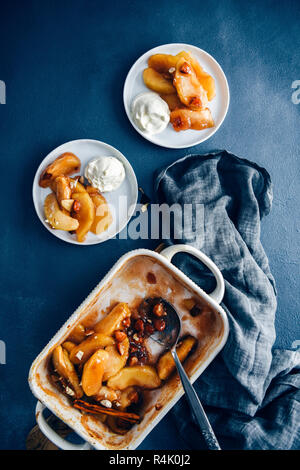 Zimt gebacken Apfelscheiben in eine Backform durch zwei weiße Platten mit gebratenen Apfelscheiben begleitet. Stockfoto