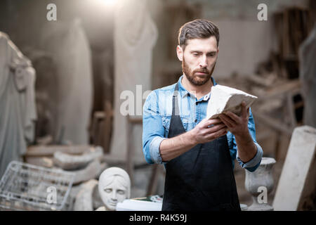 Porträt einer stattlichen Bildhauer in blauen T-Shirt und Schürze mit einem Stein im Studio Stockfoto