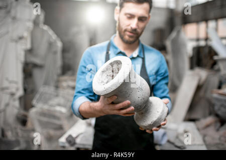Porträt einer stattlichen Bildhauer in blauen T-Shirt und Schürze Holding alte Vase im Studio mit Skulpturen auf dem Hintergrund Stockfoto