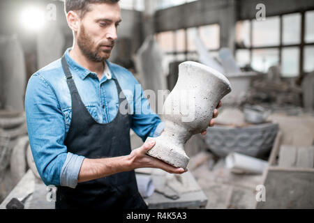 Porträt einer stattlichen Bildhauer in blauen T-Shirt und Schürze Holding alte Vase im Studio mit Skulpturen auf dem Hintergrund Stockfoto