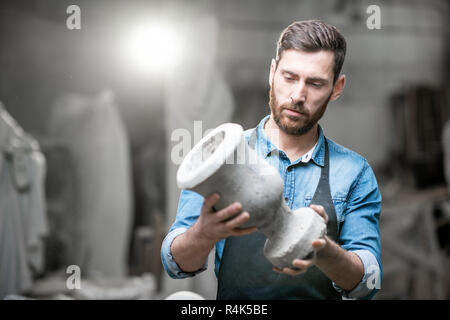 Porträt einer stattlichen Bildhauer in blauen T-Shirt und Schürze Holding alte Vase im Studio mit Skulpturen auf dem Hintergrund Stockfoto