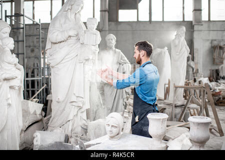 Bildhauer klatschen Hände schütteln der Staub nach der Arbeit im Studio mit Skulpturen auf dem Hintergrund Stockfoto