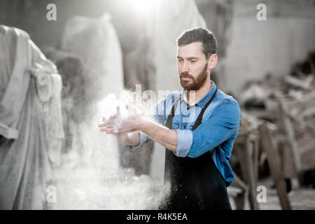 Bildhauer klatschen Hände schütteln der Staub nach der Arbeit im Studio mit Skulpturen auf dem Hintergrund Stockfoto