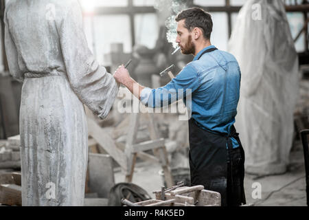 Stattliche rauchen Bildhauer schlagende Stein Skulptur mit Hammer und Meißel im Studio Stockfoto